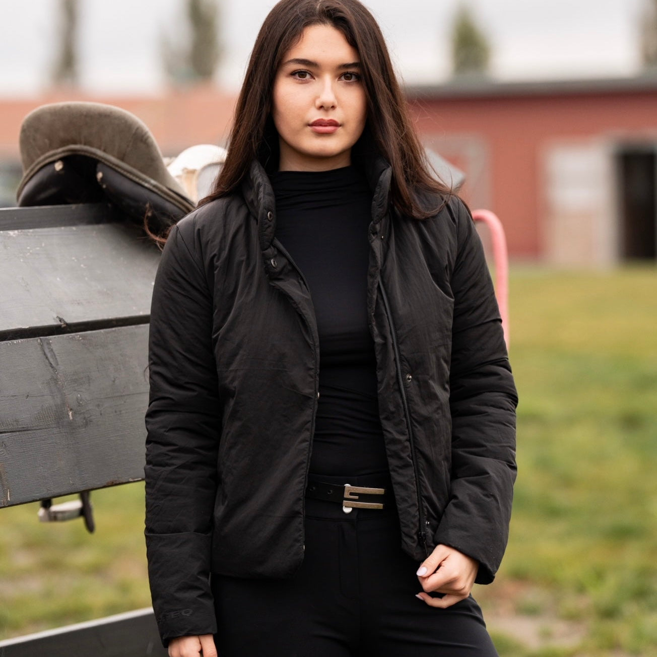Woman in black outfit with a horse saddle in an outdoor setting