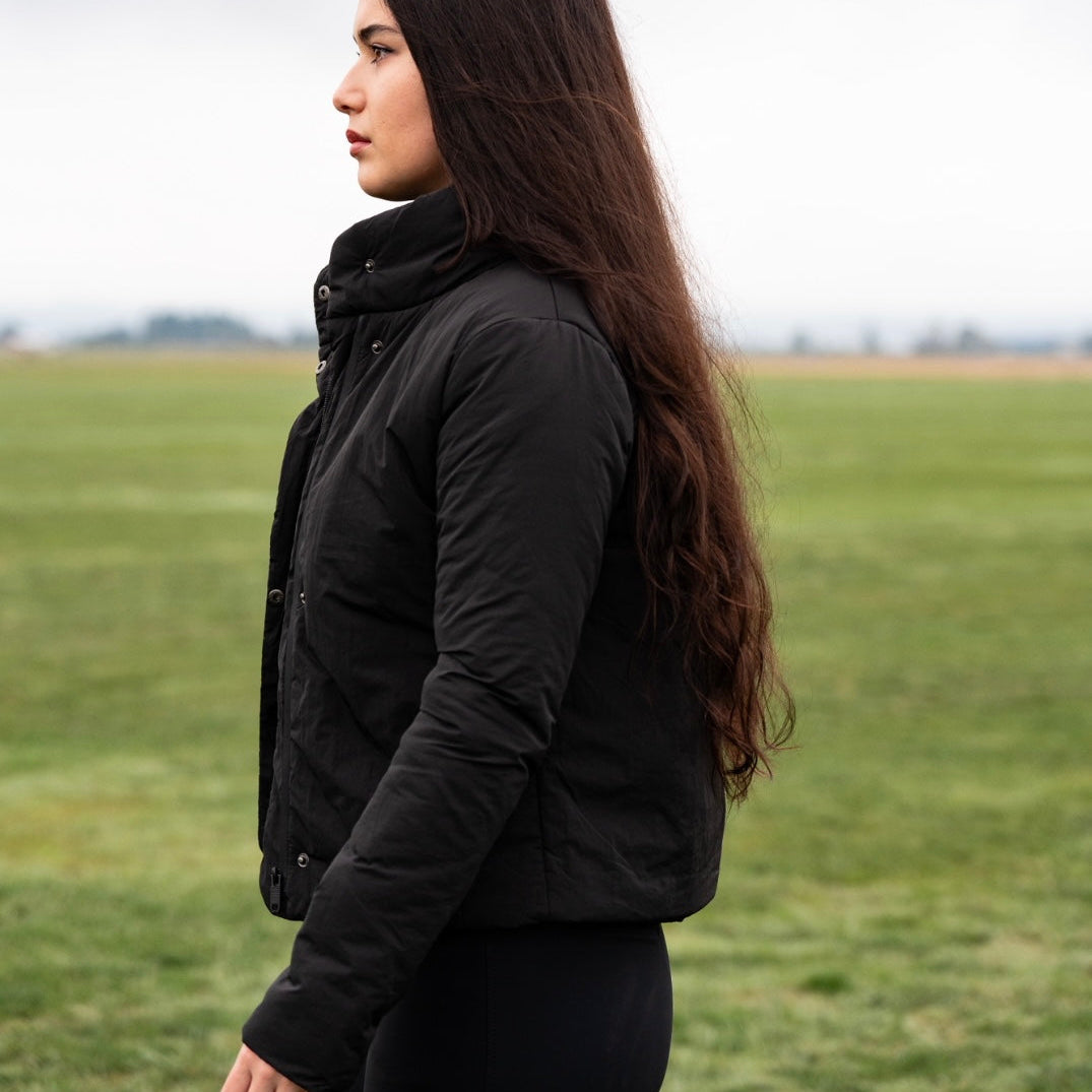 Woman wearing a black jacket standing in a grassy field