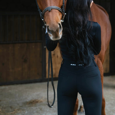 Woman standing next to a brown horse in a stable