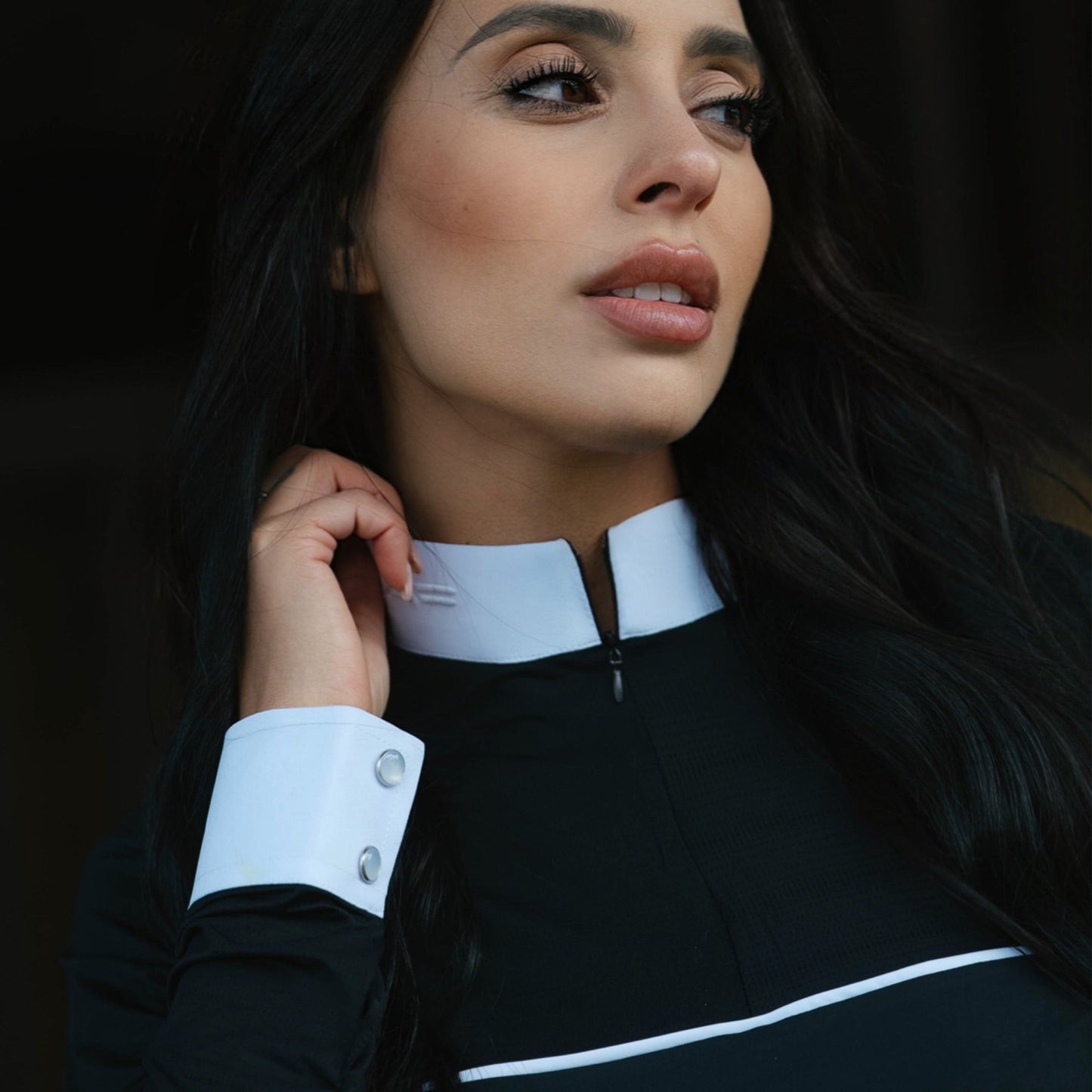 Woman wearing a black outfit with white accents against a dark background
