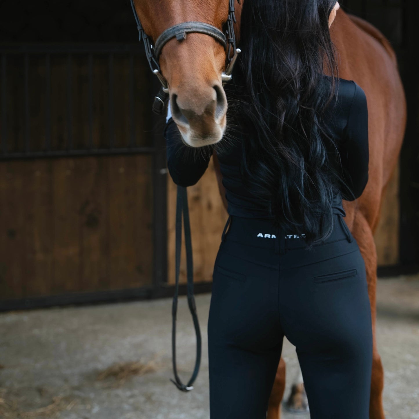 Woman standing next to a brown horse in a stable